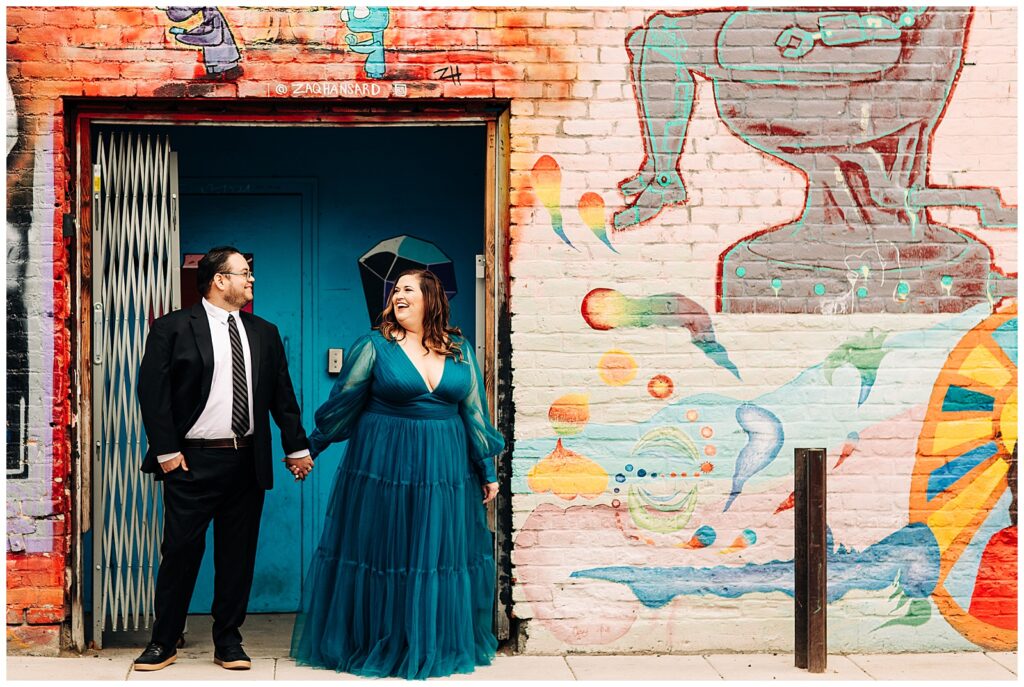 Couple standing in Freak Alley in formal outfits, surrounded by colorful street art.